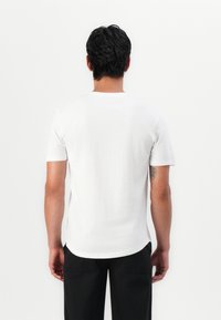 T-shirt blanc à manches courtes en coton, avec un col rond et une texture lisse, présenté de dos sur un fond uni.