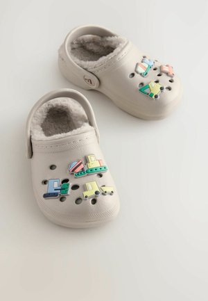 Balti klumpės su puriu pamušalu, su spalvingais, žaismingais transporto priemonių formos pakabukais ir ventiliacijos skylutėmis ant viršutinio paviršiaus.