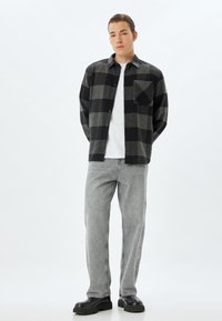 Czarna i szara, kratkowana koszula flanelowa z jedną kieszonką na piersi, zestawiona z jasnoszarymi dżinsami i czarnymi butami na platformie.