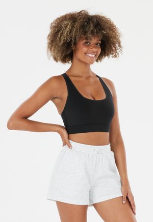 Soutien-gorge de sport noir avec un décolleté arrondi et des bretelles épaisses, associé à un short en coton gris clair avec une taille élastique et des poches latérales.