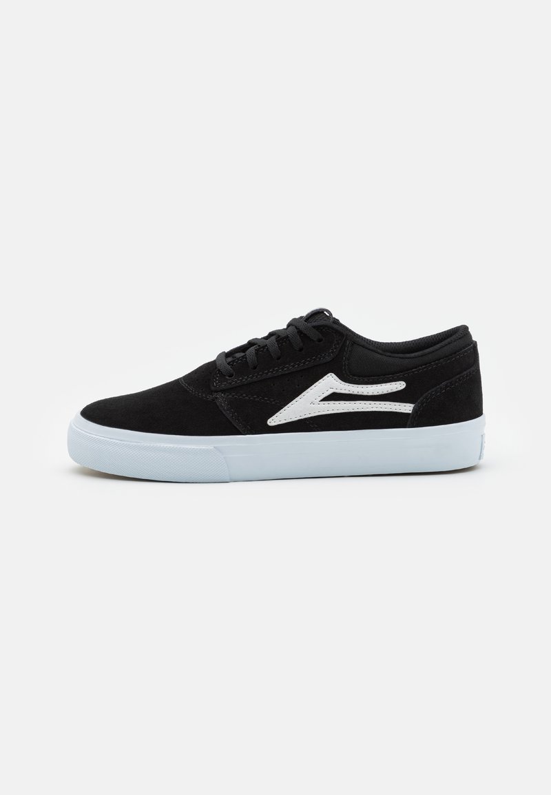 Pantofi de skate din suede negru cu accente albe, design cu șnururi, tălpi plate din cauciuc alb și o siluetă joasă.