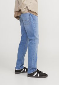Vaqueros de mezclilla azul claro con corte recto, que presentan un diseño clásico de cinco bolsillos y detalles de costura sutiles, combinados con zapatillas negras.