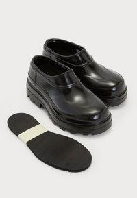 Čierne lesklé slip-on topánky s okrúhlou špičkou, hrubou podrážkou s trakciou a odnímateľnou stielkou s bielym akcentovým prúžkom.