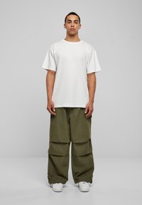 Tricou alb din bumbac cu mânecă scurtă, asortat cu pantaloni cargo cu picioare largi de culoare verde măslin, având buzunare mari și manșete ajustabile, purtat cu adidași albi.