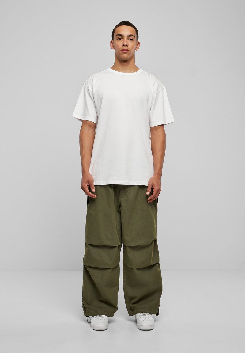 Tricou alb din bumbac cu mânecă scurtă, asortat cu pantaloni cargo cu picioare largi de culoare verde măslin, având buzunare mari și manșete ajustabile, purtat cu adidași albi.