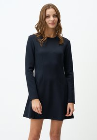 Robe noire à manches longues avec un corsage ajusté et une jupe évasée. Fabriquée en tissu doux avec une texture subtile, dotée de coutures latérales et d'un col rond.