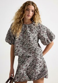 Paita dengan lengan bengkak dan rok yang serasi terbuat dari kain bertekstur, menampilkan pola abstrak hitam, putih, dan pink. Hem pendek dan melebar.