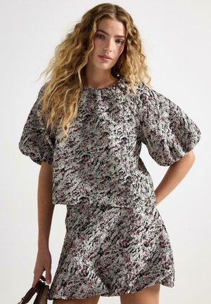 Top med puffærmer og matchende nederdel i struktureret stof, prydet med et abstrakt mønster i sort, hvid og lyserød. Kort, udvidet kant.