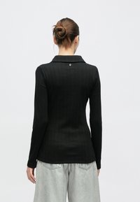 Μαύρο ριμπ μακρυμάνικο πουκάμισο με γιακά και λεπτομέρεια ενός κουμπιού στην πλάτη. Φορεμένο με ανοιχτό ασημί μεταλλιζέ παντελόνια. Ομαλή υφή.