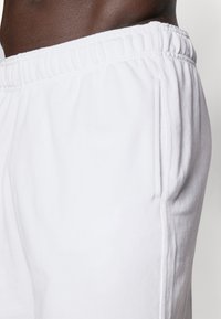 White sweatpants with a ribbed elastic waistband and side pockets. Made of soft cotton fabric, featuring stitched seams along the sides.