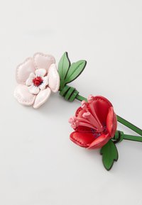 Dwa kwiatowe spinki do włosów wykonane z teksturowanej skóry; jedna różowa z czerwonymi akcentami, druga czerwona z różowymi pręcikami, obie z zielonymi liśćmi.