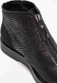 Botín negro hasta el tobillo con piel de reptil texturizada, cremallera lateral y acentos de ante. Suela de goma plana, con acabados lisos y mate.