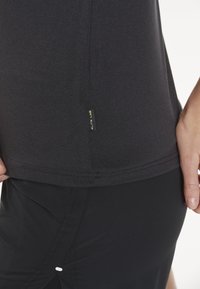 Zwart sportshirt met een soepele textuur, korte mouwen en een zijlabel. Gepaard met zwarte, aansluitende shorts met een kleine witte accent.