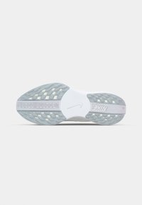Hvid sneaker sål med tekstureret grå gummi, der har et mønstret dækmønster og et centralt logo. Accenter inkluderer synlige polstreelementer.