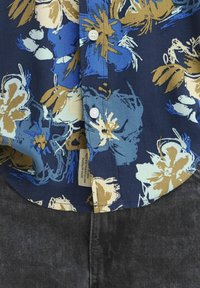 Cămașă cu butoni florală, fundal albastru marin cu flori de culoare albastru deschis, crem și auriu. Prezintă butoni albi și etichetă din material la tiv.