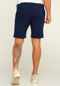Marineblaue Baumwollshorts mit lockerer Passform, elastischem Bund und dekorativen Nähten; getragen mit hellen Slippern.