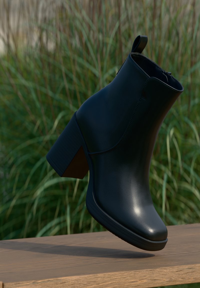 Bottine en cuir noir à talon bloc flottant au-dessus d'une surface en bois, avec de l'herbe verte floue en arrière-plan.