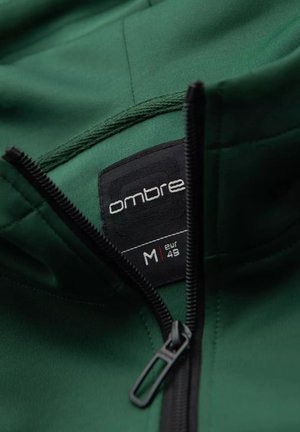 Zielona bluza z kapturem z czarną etykietą z napisem "ombre" oraz rozmiarem "M" (EUR 48). Posiada zamek błyskawiczny oraz gładki, teksturowany materiał.
