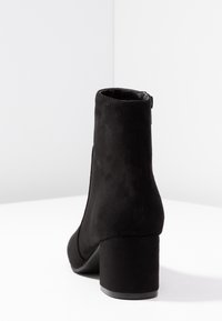 Stivaletto in suede nero con tacco a blocco, texture liscia e punta rotonda. Presenta una chiusura con zip sul retro e un design minimale.