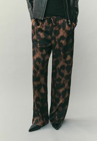 Könnyű, fekete és barna leopárdmintás nadrág gumis derékrésszel, oldalzsebekkel és laza szabással, hegyes orrú fekete cipővel párosítva.