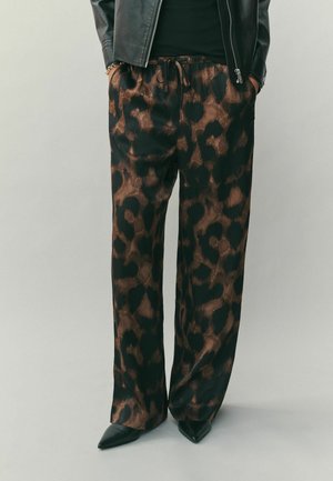 Leichte, schwarze und braune Leopardenmuster-Hose mit elastischem Bund, seitlichen Taschen und lockerer Passform, kombiniert mit schwarzen Spitzenschuhen.