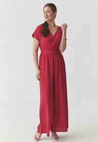 Tuta rossa a trama con scollo a V, maniche corte e vita legata. Fit largo e fluido. Abbinata a sandali con cinturini di colore chiaro.