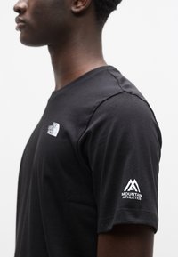 Μαύρο βαμβακερό t-shirt με στρογγυλή λαιμόκοψη και κοντά μανίκια, με λευκό λογότυπο στο στήθος και λευκό λογότυπο "Mountain Athletics" στο μπράτσο.