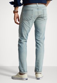 Vaaleansiniset farkut, joissa on slim fit -leikkaus, takataskut, huomaamaton ompelu ja vyö. Vaatteen kanssa on vaaleat kengät.