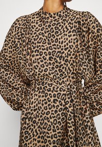 Leopardenmuster-Kleid mit hohem Kragen, gepufften Ärmeln und gebundenem Taillengürtel. Hergestellt aus glattem, leichtem Stoff in Beige- und schwarzen Farben.