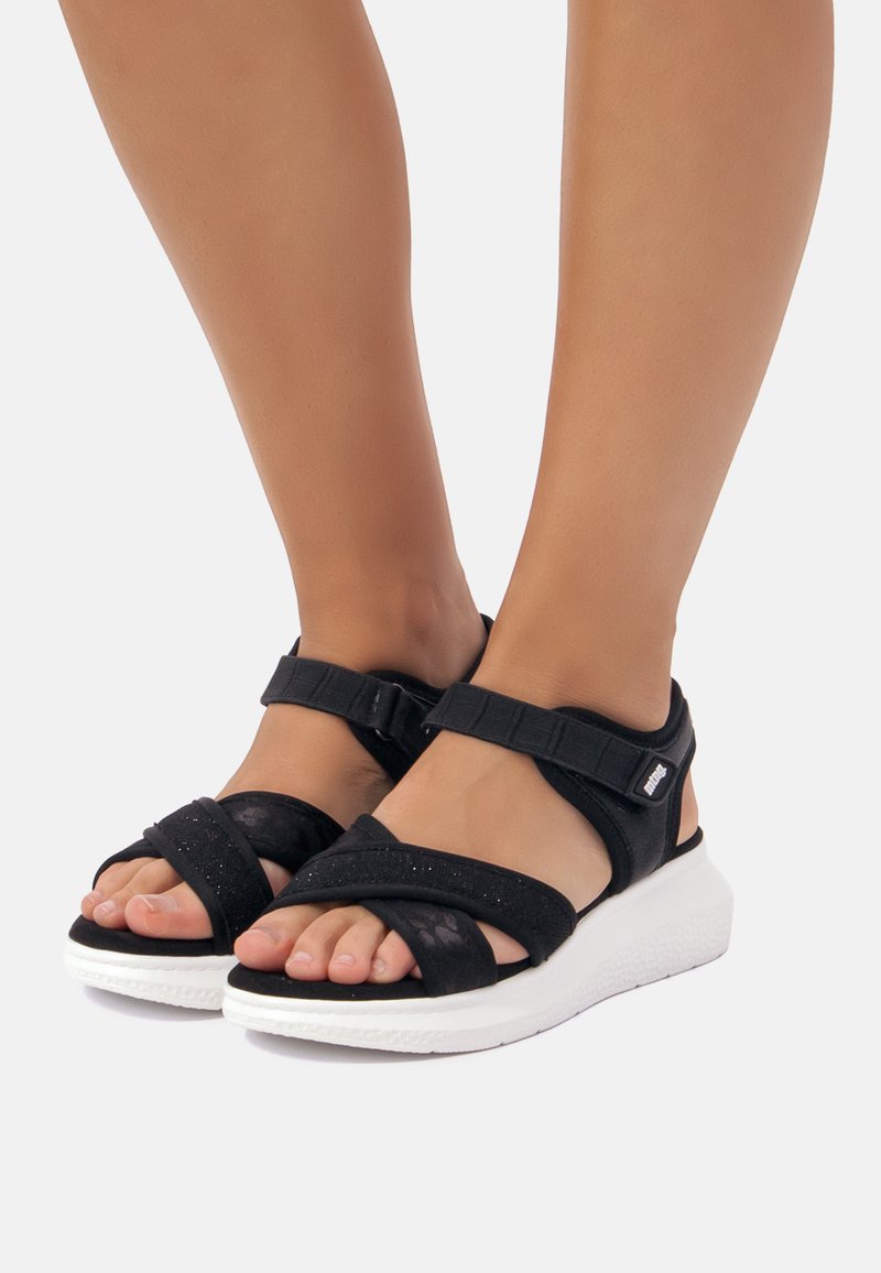 Sandali neri con cinturini regolabili, dotati di una tomaia testurizzata, chiusura in velcro e suola piatta bianca.