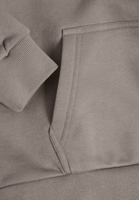 Grauer Hoodie-Stoff mit gerippten Bündchen und Saum. Kängurutasche mit schrägen Nähten. Weiche Textur, minimalistisches Design und neutrale Farbe.