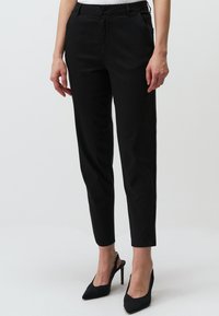 Zwarte taps toelopende broek van katoen, met voorzakken, een knoopsluiting en een gladde textuur, gecombineerd met spitse zwarte hakken.