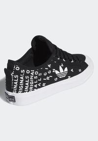 Svart canvas-sneaker med vittryckt text och logotyp. Har en vit gummisula och svarta snören. Texten inkluderar "ORIGINALS" och "ADIDAS."
