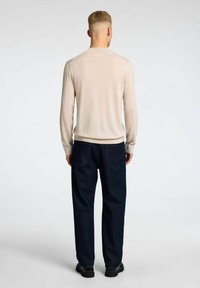 Maglione beige a maniche lunghe con orlo e polsini a costine, abbinato a jeans in denim blu scuro, larghi. Design semplice con dettagli minimi.