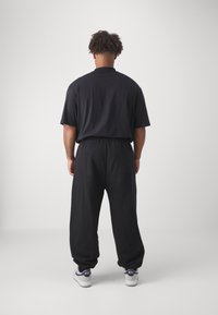 Schwarzes T-Shirt mit kurzen Ärmeln, kombiniert mit schwarzen Jogginghosen mit einem elastischen Bund. Weiße Sneakers mit navyblauen Akzenten.