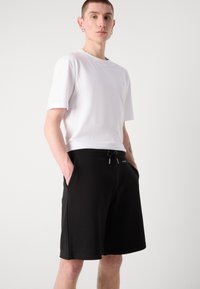 Bílý tričko s kulatým výstřihem kombinované s černými sportovními šortkami s elastickým pasem, šňůrkou a bočními kapsami. Minimalistický design.