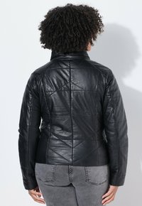 Giubbotto di pelle nera con motivo trapuntato, dotato di un colletto alto, design aderente e maniche lunghe, mostrato da dietro.