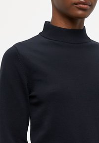 Jūras spēku turtlenecks džemperis, kas izgatavots no mīksta trikotāžas auduma, ar pieguļošu dizainu, augstu apkakli un minimālistiskām šuvēm uz piedurknēm.
