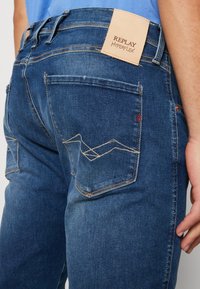 Jeans de mezclilla en azul oscuro con un acabado texturizado. Presentan una etiqueta de cuero con marca y un distintivo pespunte en zigzag en los bolsillos traseros.
