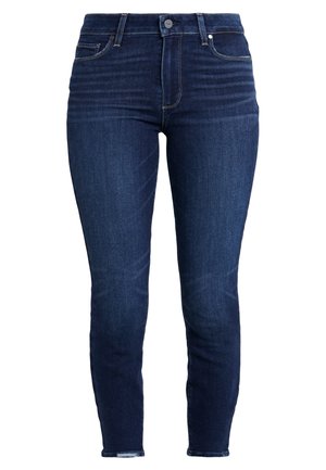 Tummansiniset skinny-farkut korkealla vyötäröllä, edessä napitus, vetoketju ja viiden taskun muotoilu, jossa hillittyä haalistumista ja ompelu yksityiskohtia.