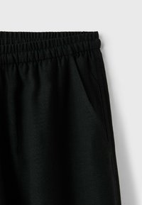 Pantalon à taille élastique noire avec poche latérale visible sur un fond blanc uni.