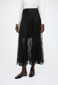 Μαύρη midi φούστα από δαντέλα με στρωματοποιημένο σχέδιο, με υφή, εφαρμοστή μέση και φουσκωτή σιλουέτα. Συνδυασμ ένη με μαύρες μπαλαρίνες.