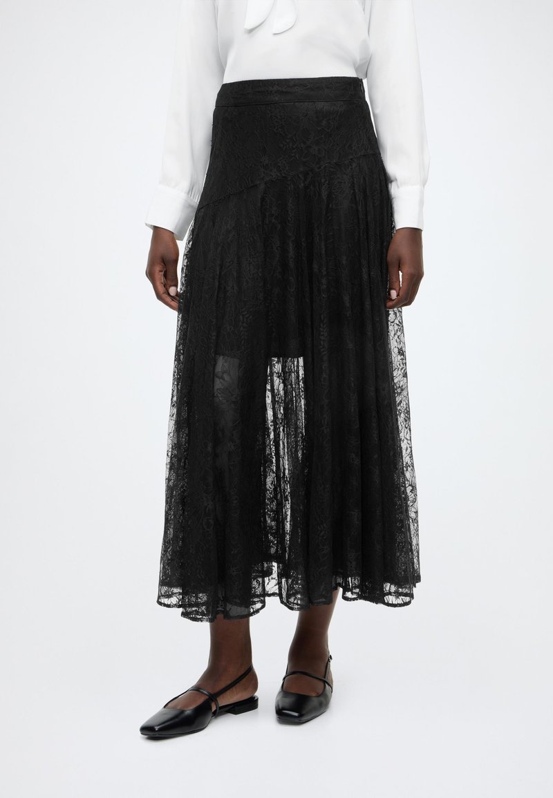 Μαύρη midi φούστα από δαντέλα με στρωματοποιημένο σχέδιο, με υφή, εφαρμοστή μέση και φουσκωτή σιλουέτα. Συνδυασμένη με μαύρες μπαλαρίνες.
