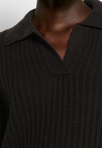 Suéter negro de punto acanalado con escote en V y cuello. Presenta una textura de tela y un sutil detalle en las costuras.