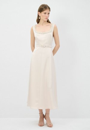 Une robe sans manches, crème, avec un décolleté carré orné de perles, une taille cintrée et un accent ceinturé, présentant une jupe fluide.