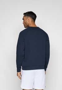 Felpa girocollo blu navy con maniche raglan e polsini a coste. Tessuto liscio, vestibilità comoda e design minimalista.