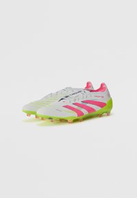 Botas de fútbol Predator, con un cuerpo blanco y acentos en rosa y verde, superficie texturizada y tacos translúcidos rosa.