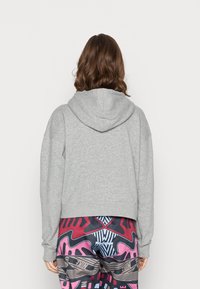 Sudadera de algodón gris con capucha ajustable, corte holgado y mangas largas, llevada sobre leggins de patrón colorido con diseños en rosa, azul y negro.