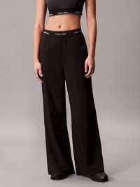 Calças largas pretas com uma textura suave e um cós elástico que apresenta um logótipo da Calvin Klein em branco contrastante.
