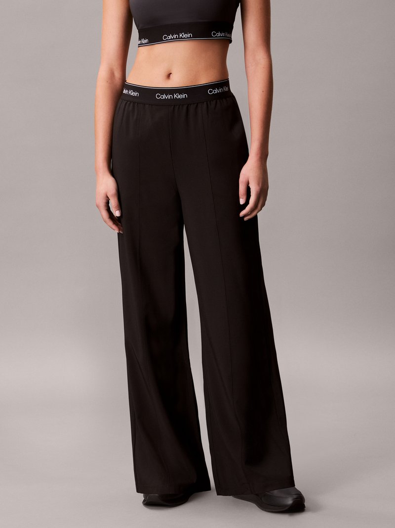 Calças largas pretas com uma textura suave e um cós elástico que apresenta um logótipo da Calvin Klein em branco contrastante.
